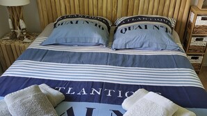 Una cama con ropa de cama a rayas, dos almohadas con texto y dos toallas dobladas.