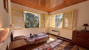 A cozy bedroom with a wooden ceiling, large windows with shutters, a bed with a patterned bedspread, a bedside table, and a dresser with a lamp. - 2-room apartment near beach with garden in Saint Aygulf (Saint-Aygulf)