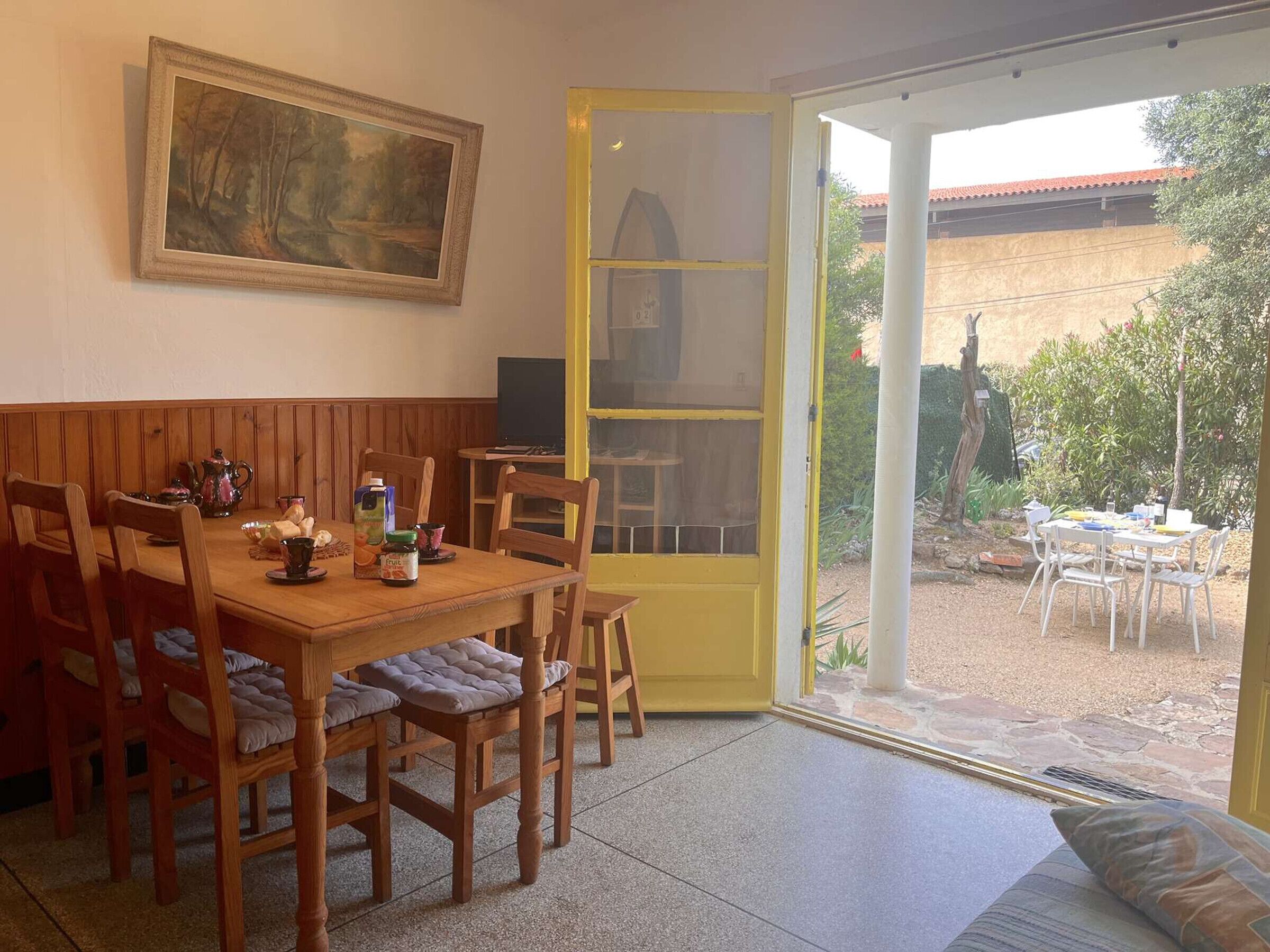 Un comedor con una mesa y sillas de madera, un cuadro en la pared y vistas al jardín a través de un ventanal.
