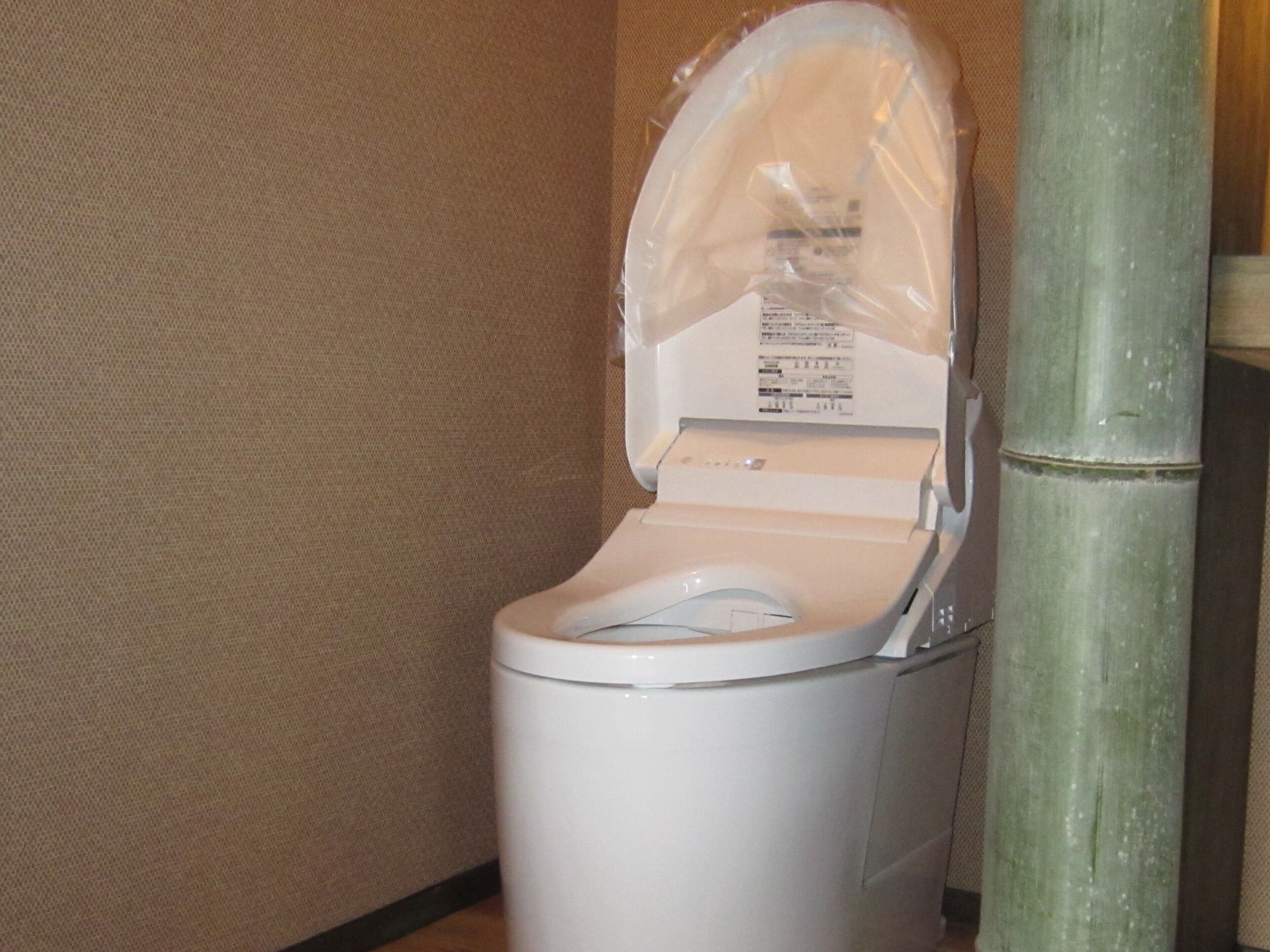 A white toilet with a plastic cover over the seat, positioned next to a bamboo pillar.