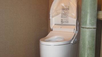 A white toilet with a plastic cover over the seat, positioned next to a bamboo pillar.