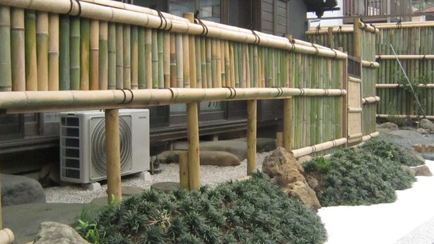 A traditional Japanese building with a bamboo fence, a stone lantern, and a small garden with rocks and plants. - Marina bay Numazu (Numazu)