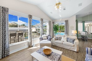 A spacious living area with a large window, a white sofa, a coffee table, and a dining area with chairs and a table. - Beach feeling from the first day (Cape Coral)