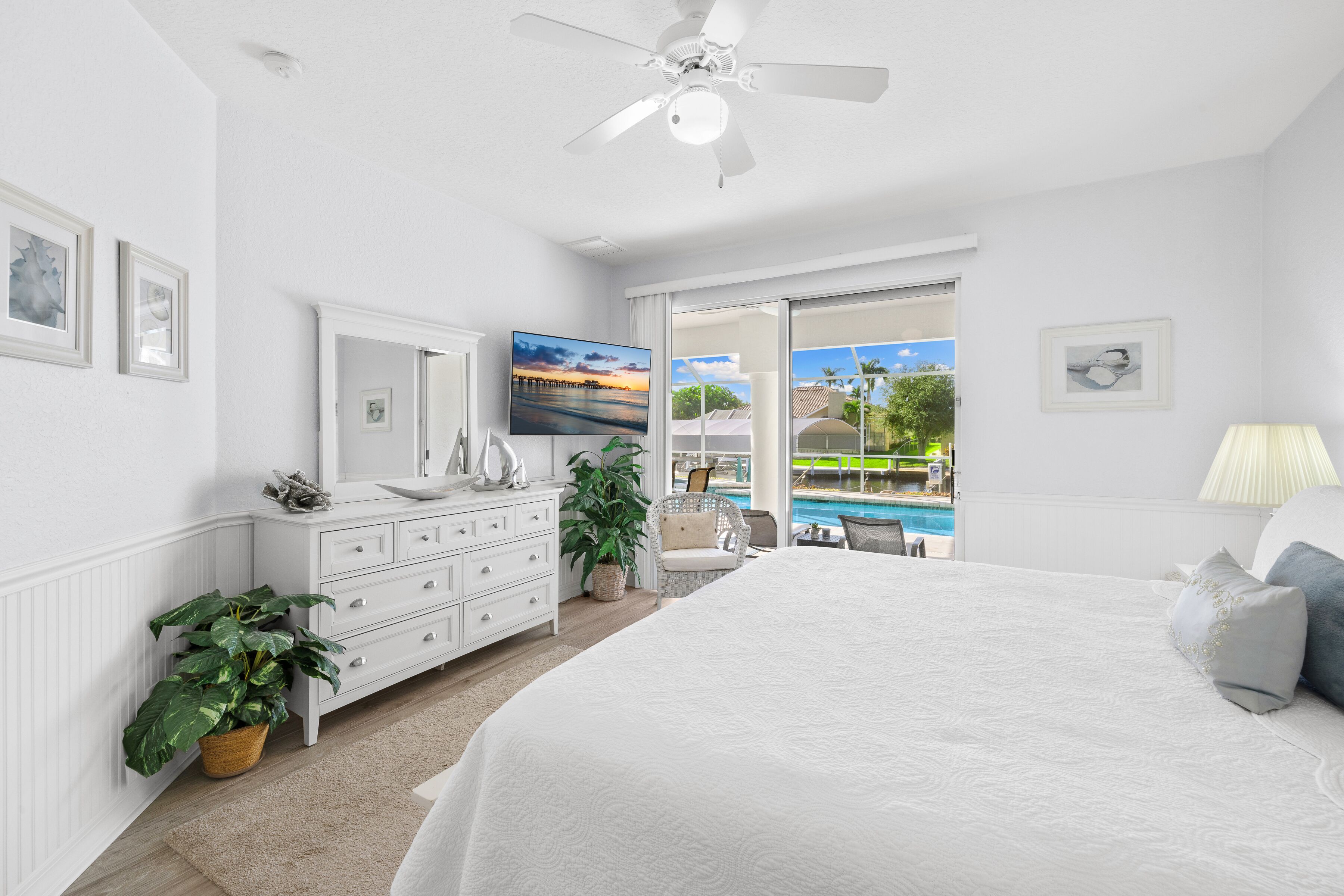 A bedroom with a large bed, a dresser, a ceiling fan, and a view of a swimming pool.