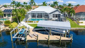 Ein modernes Haus mit großem, verglasten Pool, einem am Steg vertäuten Boot und freiem Blick auf die umliegende Nachbarschaft.