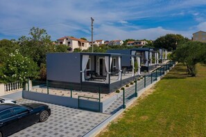 Una fila di case mobili moderne a un piano, con aree salotto all’aperto, vialetto lastricato e un’auto parcheggiata davanti.