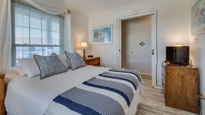 A bedroom with a large bed, a nightstand, a television, and a door leading to another room. - Summer Breeze 312 1 Bedroom Condo by RedAwning (Miramar Beach)