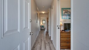 A hallway with white doors, a wooden floor, and a bed in the distance. - Summer Breeze 312 1 Bedroom Condo by RedAwning (Miramar Beach)
