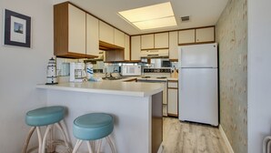 A compact kitchen with a central island, two bar stools, and a refrigerator. - Summer Breeze 312 1 Bedroom Condo by RedAwning (Miramar Beach)