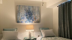 Ein Zimmer mit zwei Betten, einem Deckenventilator, einem Bild an der Wand und einer Lampe auf einem kleinen Tisch.