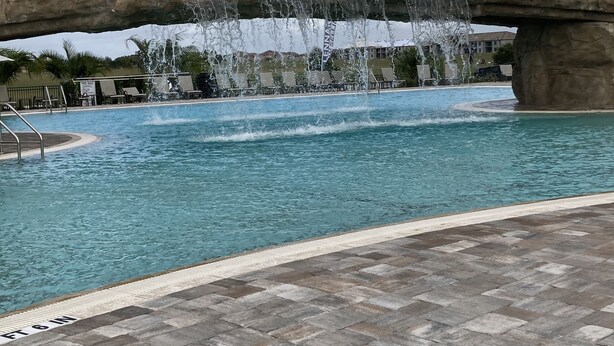 Ein Pool mit Wasserfall, Liegestühlen und einer Steinbrücke.