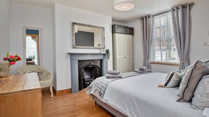 A bedroom with a bed, a dresser, a chair, a fireplace, and a wardrobe. - Oystercatcher (Whitby)