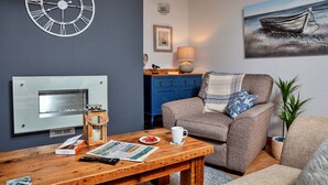 A living room with a fireplace, a clock, a painting, and a cozy seating area. - Oystercatcher (Whitby)