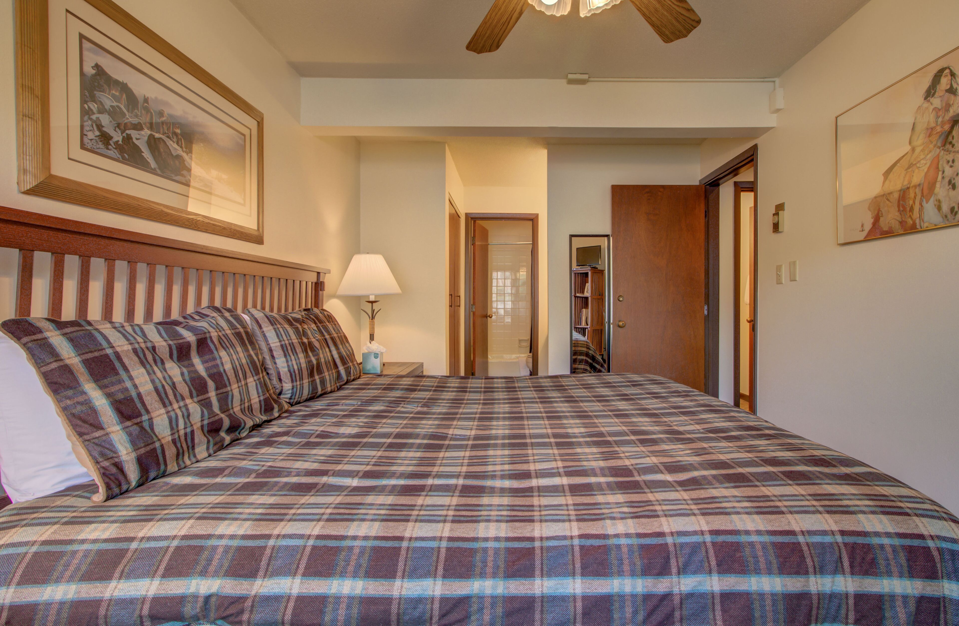 A bedroom with a plaid bedspread, a nightstand with a lamp, and framed artwork on the walls.