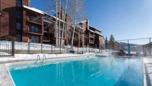 Una piscina azul cristalina junto a un edificio con varios balcones y suelo cubierto de nieve.