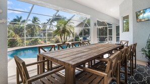 A wooden dining table with chairs, a pool, and a view of palm trees and a house through large windows. - /\ Amazing Location/\ 10 mins away from beach and Mercato/ New Diamond in Naples (Naples)