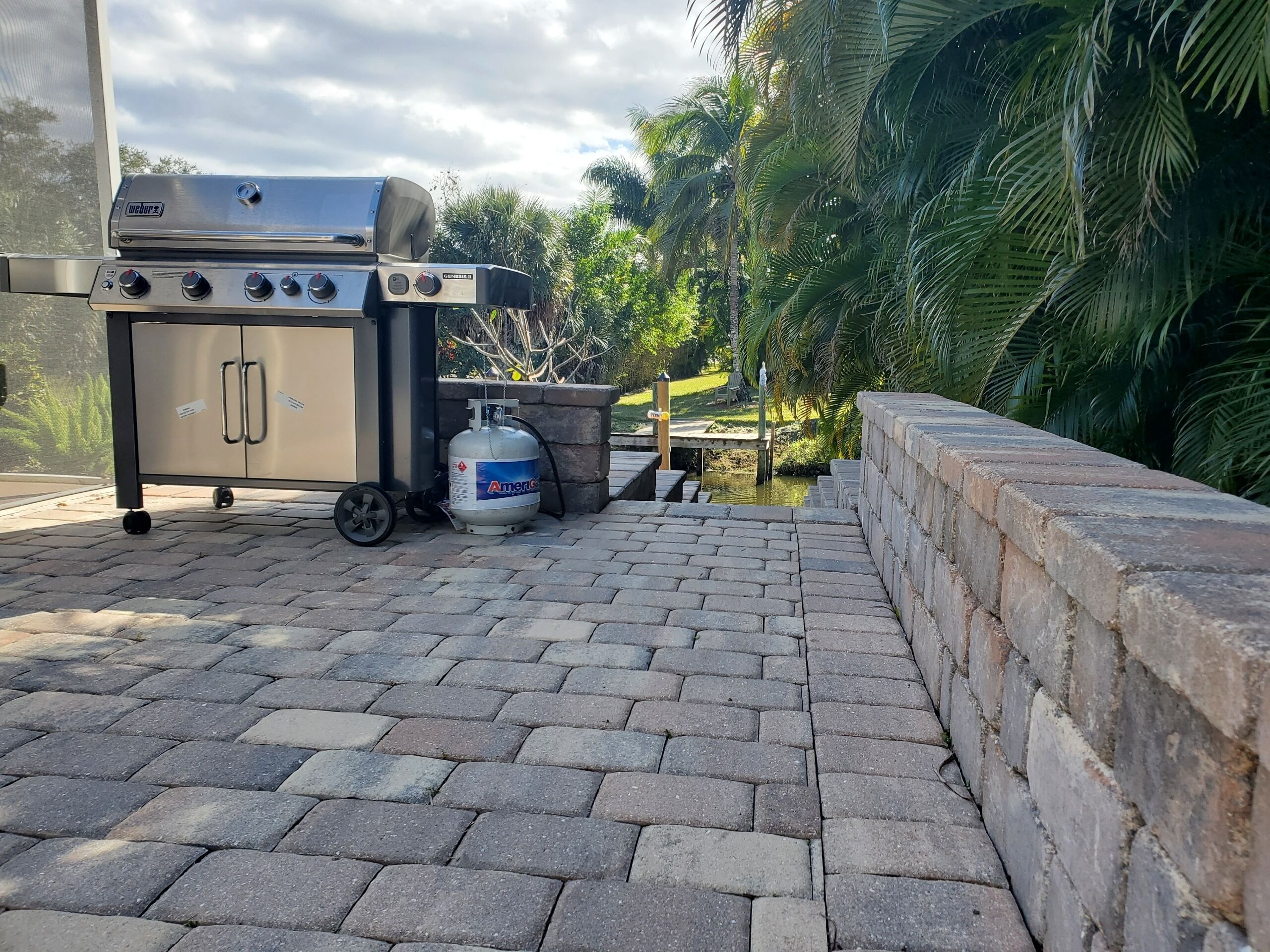 A portable Weber grill with a propane tank on a paved patio.