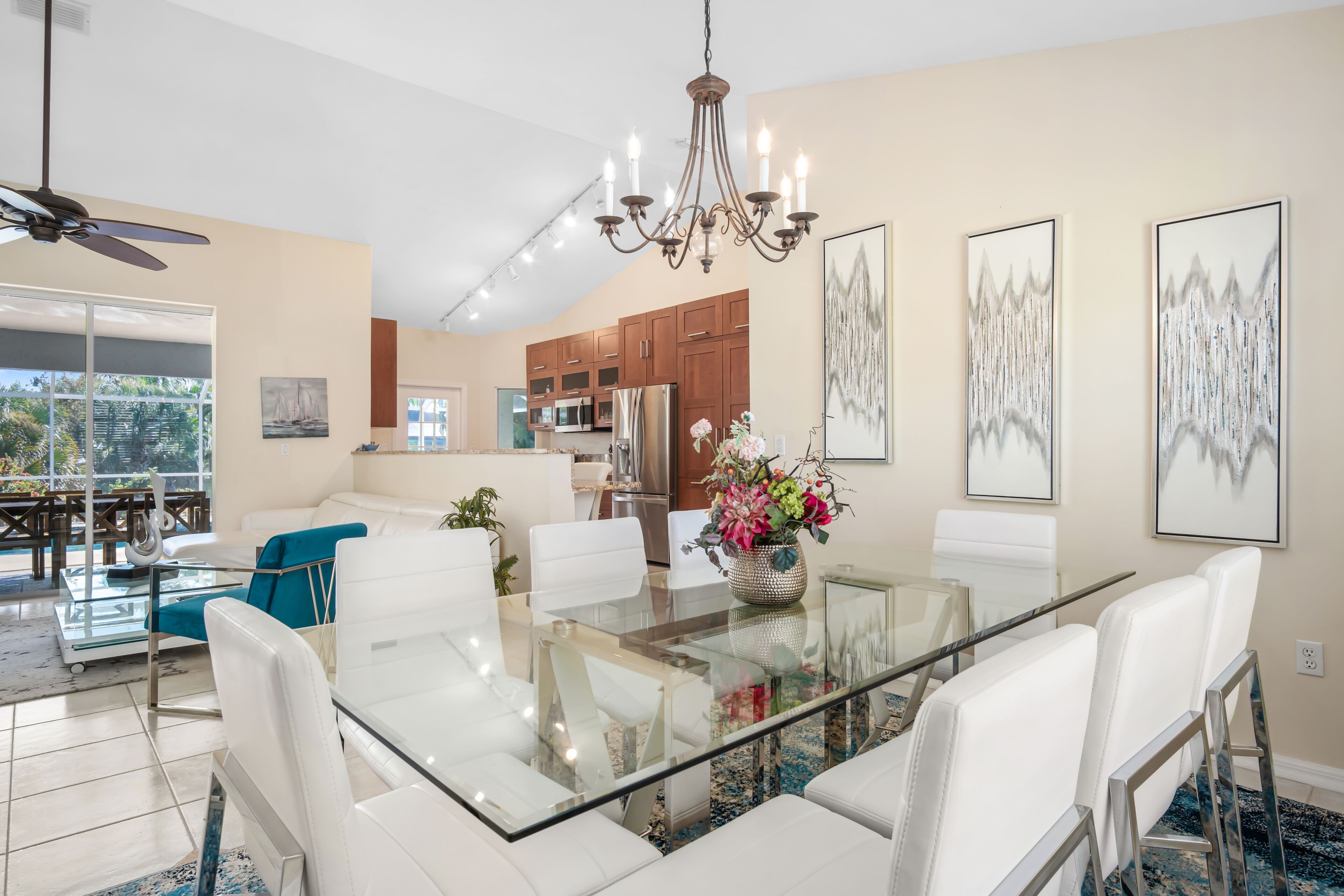 A modern dining area with a glass-top table, white chairs, and a chandelier.