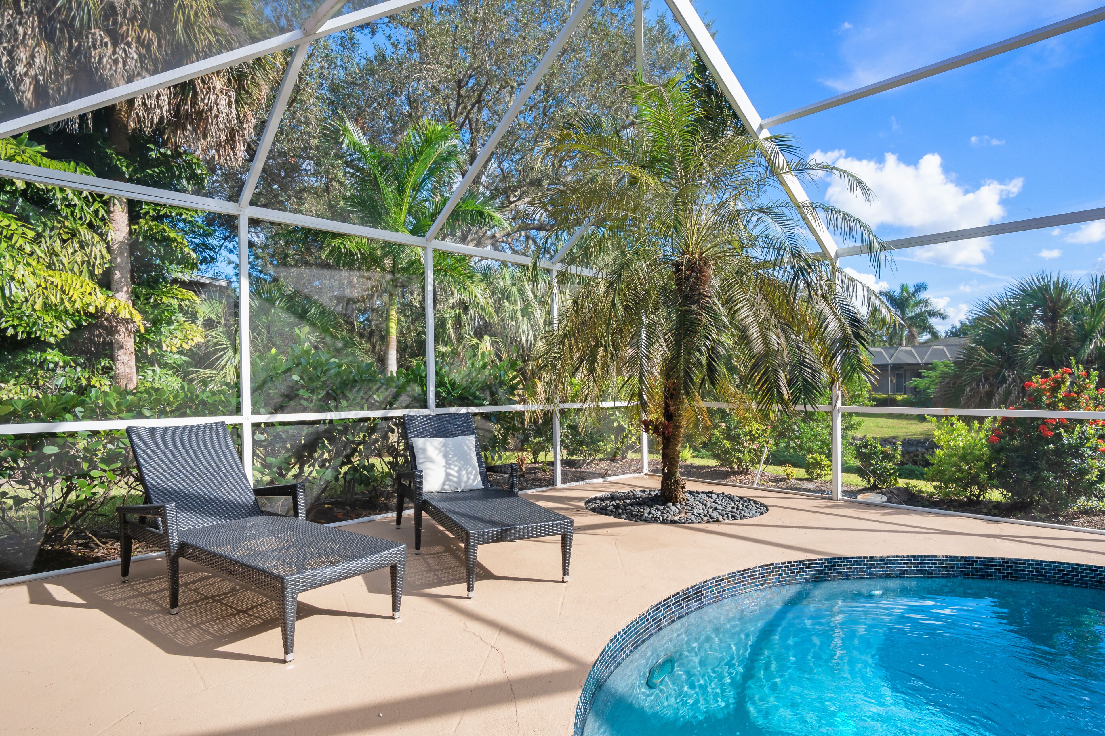 Un área de piscina interior con dos sillas reclinables, una palmera y vistas de la vegetación circundante.