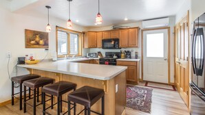Cocina moderna con armarios de madera, una isla grande con taburetes de bar, iluminación colgante y un refrigerador.