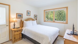 Une chambre à coucher avec un lit, une table de chevet, une lampe et une fenêtre donnant sur des arbres.