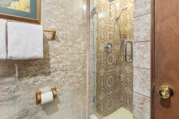 Un bagno con piastrelle decorate, cabina doccia in vetro, porta asciugamani in legno e porta rotolo carta igienica.