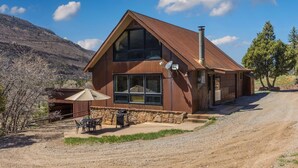 A two-story house with a stone foundation, large windows, and a chimney. - Rustic Cabin | Great Views | Close to Downtown Ouray | STR2025-067 (Ridgway)