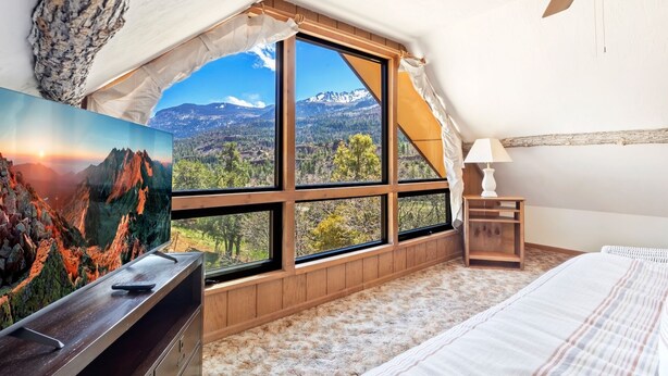 A bedroom with a large window offering a mountain view, a bed, a nightstand, and a painting on the wall. - Rustic Cabin | Great Views | Close to Downtown Ouray | STR2025-067 (Ridgway)