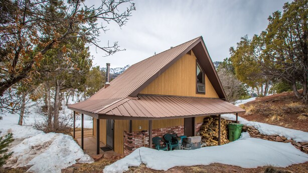 A wooden cabin with a sloped roof, a covered porch, and a stone foundation.