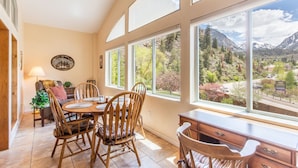 A dining area with a table and chairs, large windows with a mountain view, and a cozy interior with wooden furniture. - Unbeatable Location | Across from Ouray Hot Springs | Walk to Downtown (Ouray)