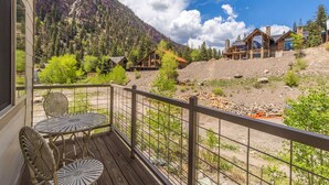 A wooden deck with outdoor seating, overlooking a mountainous landscape with multiple buildings. - Unbeatable Location | Across from Ouray Hot Springs | Walk to Downtown (Ouray)
