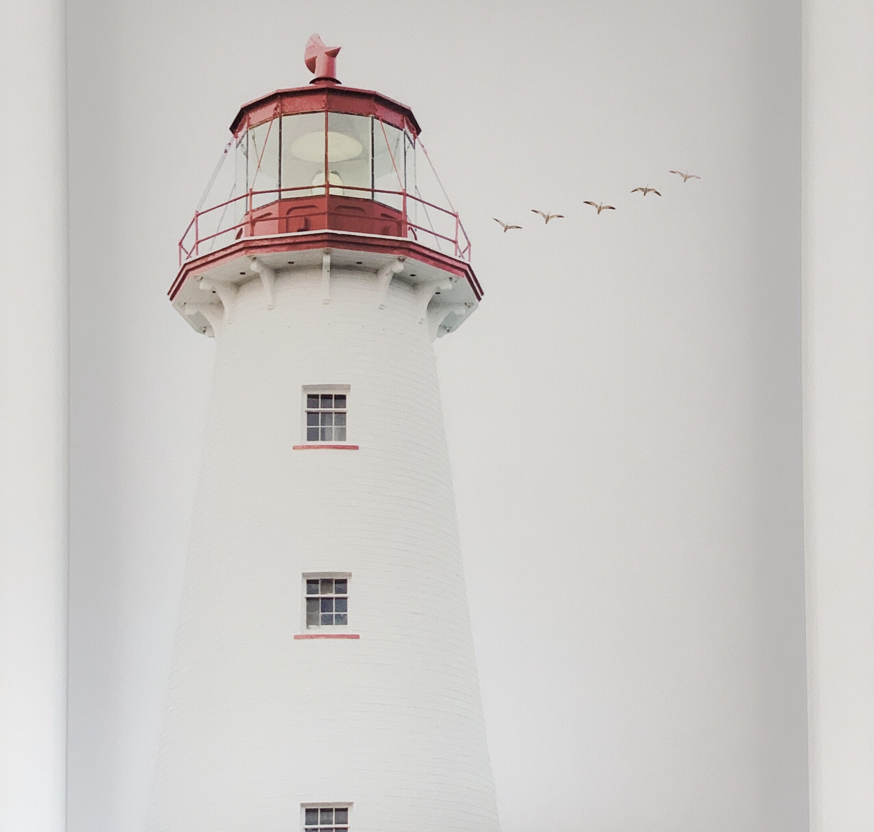 A tall white lighthouse with red accents and multiple windows.