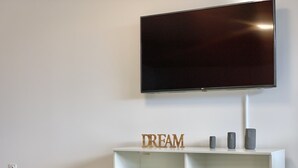 A modern living room with a flat-screen TV mounted on the wall, a white entertainment unit with the word "DREAM" on it, and a remote control on a black couch. - #AV | The Ladybug 🐞| Terrace |Tout équipé (Meylan)