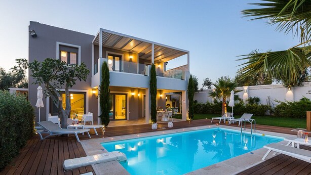Een modern huis met twee verdiepingen, een zwembad, tuinmeubilair en een goed verlicht terras.