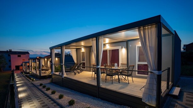 Ein moderner Außenbereich mit Glasveranda, Esstisch, Stühlen und einem kleinen Garten.