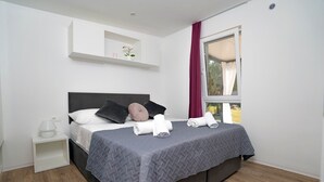 Ein modernes Schlafzimmer mit Bett, Kissen, einem Nachttisch, einem Fenster mit Vorhängen und einem kleinen Regal mit einer Pflanze.