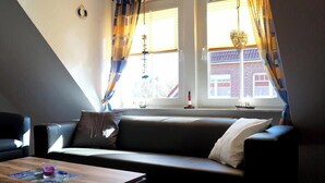 Ein modernes Wohnzimmer mit einer Couch, einem Couchtisch und Blick auf ein Gebäude durch große, mit Vorhängen versehene Fenster.