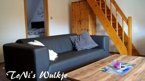 Ein Wohnzimmer mit einem schwarzen Sofa, einem Holztisch mit einem Glas und einer Holztreppe.