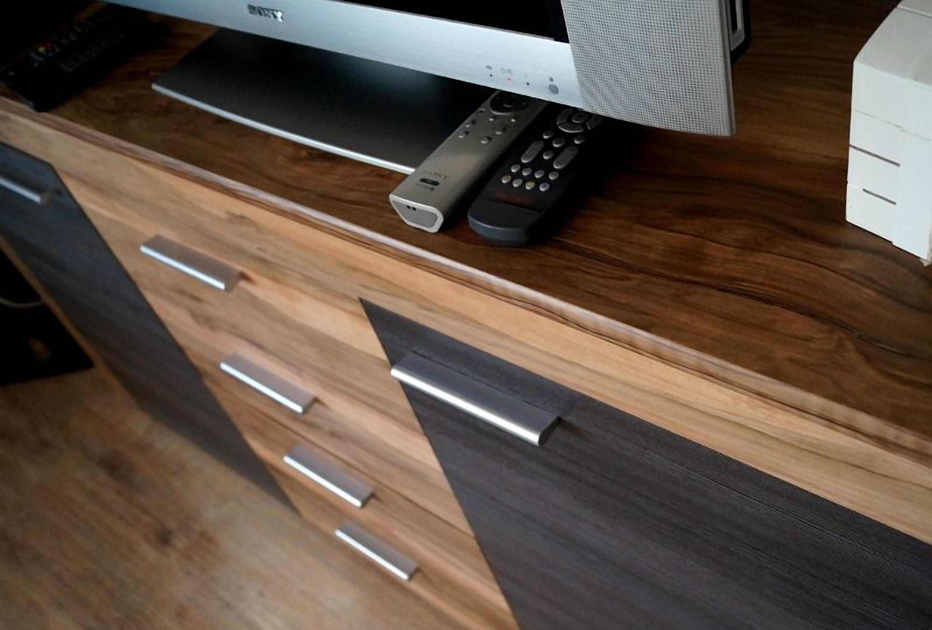 Een houten entertainmentkast met een flatscreen-televisie, afstandsbedieningen en een speaker.