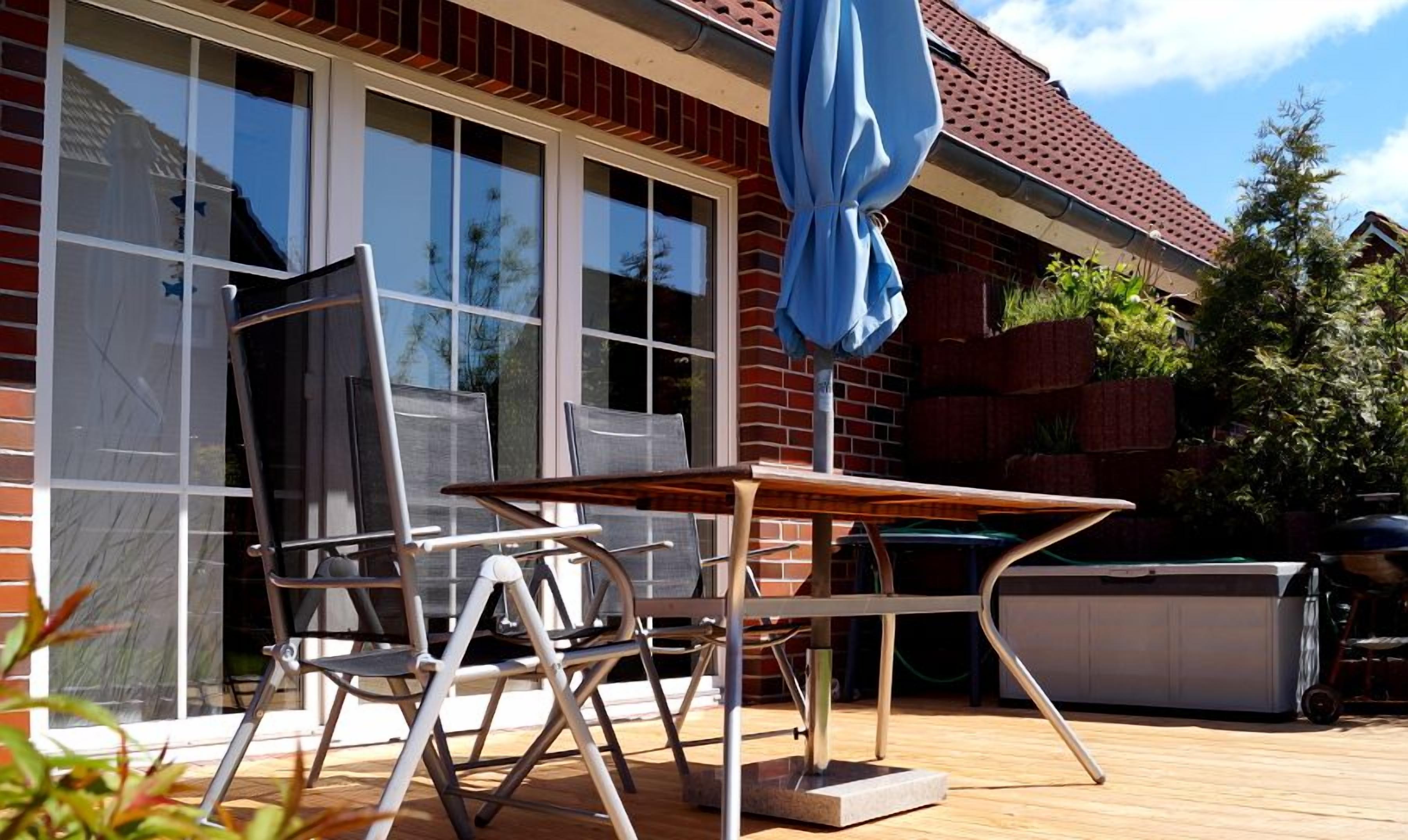 An outdoor patio with a table and chairs, a blue umbrella, and a hot tub.