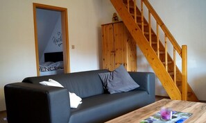Una sala de estar con un sofá negro, una mesa de madera con un vaso, y una escalera de madera.