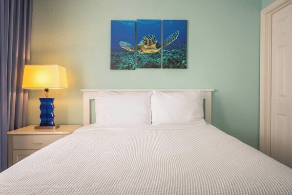 A hotel room with a bed, a nightstand with a lamp, and a wall-mounted painting of a sea turtle.