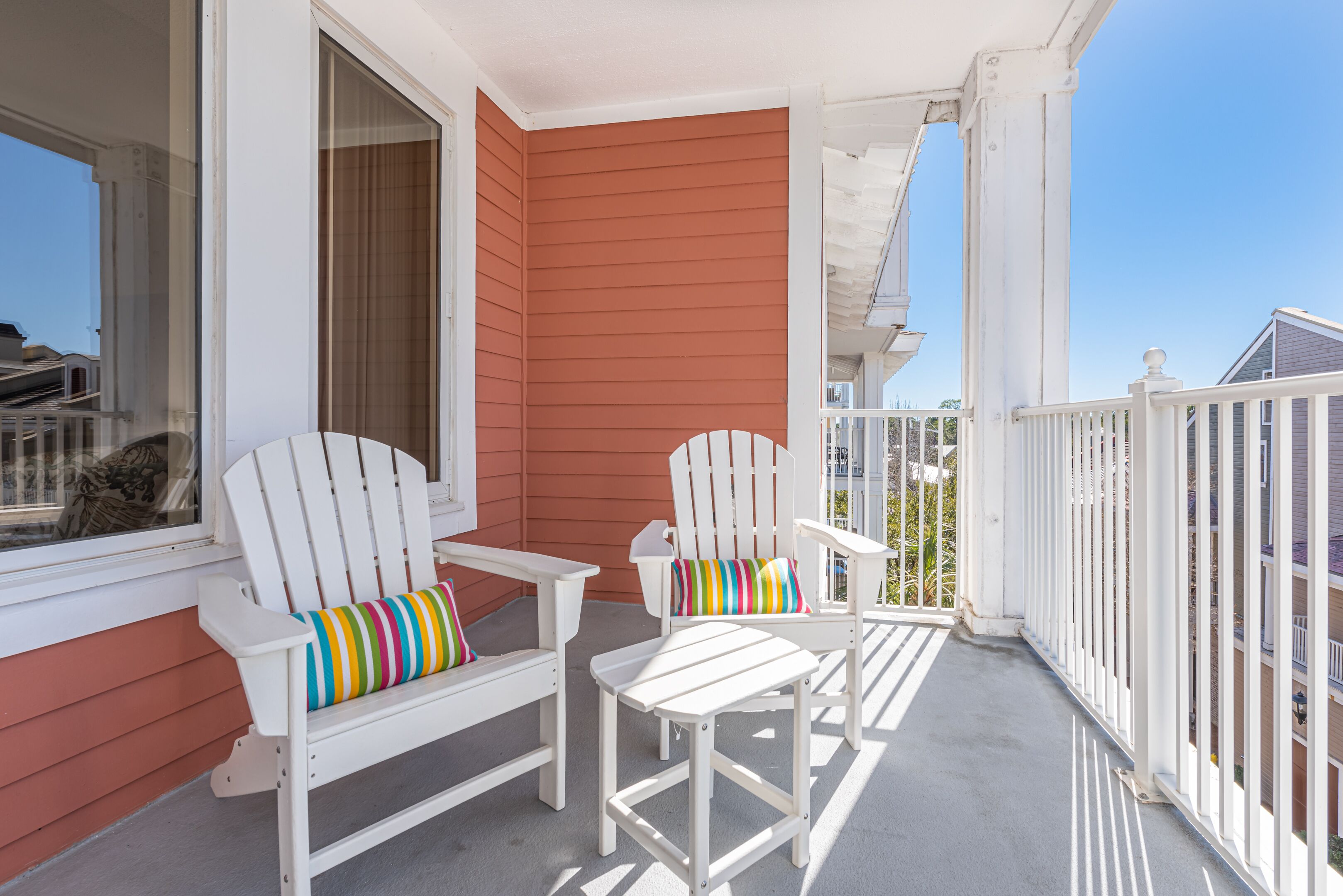 A porch with two white Adirondack chairs, one with a colorful striped pillow.