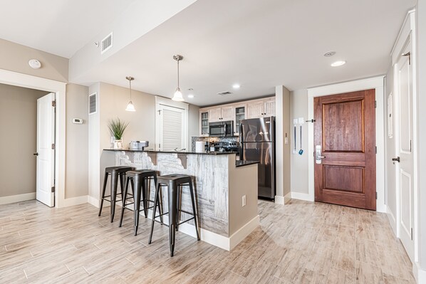 A modern kitchen with a central island, bar stools, stainless steel appliances, and a wooden door.