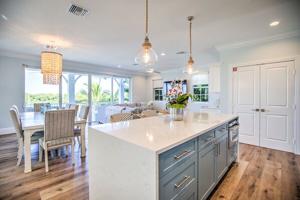 A modern kitchen with a large island, pendant lighting, and a view of the outdoors.
