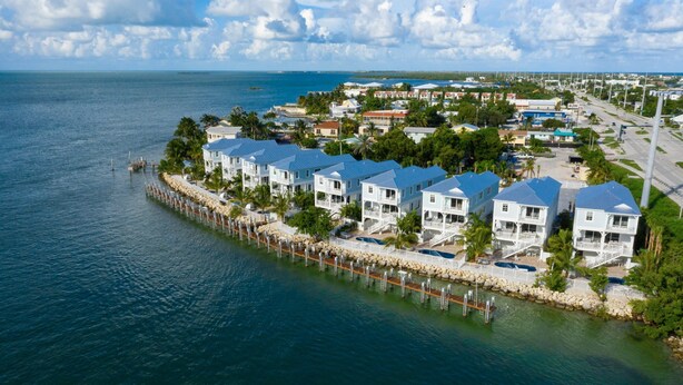A waterfront property with multiple white buildings, a dock, and a view of the ocean. - Stunning **BRIGHT** Direct Waterfront 5/4 Home! Private Pool, Hot Tub & Dock! (Marathon)