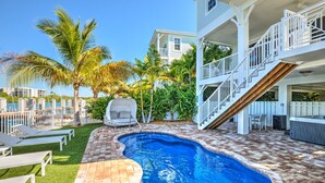 A swimming pool with a wooden deck, a covered seating area, and a two-story building with a balcony. - Stunning **BRIGHT** Direct Waterfront 5/4 Home! Private Pool, Hot Tub & Dock! (Marathon)