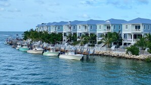 A waterfront property with multiple-story buildings, a dock with several boats, and a rocky shoreline with palm trees. - Stunning **BRIGHT** Direct Waterfront 5/4 Home! Private Pool, Hot Tub & Dock! (Marathon)