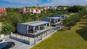 A modern hotel with a covered outdoor area, a paved driveway, and a view of surrounding residential buildings. - Adriatic Mobile Homes 3 (Sveti Filip i Jakov)
