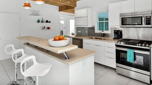 A modern kitchen with white cabinets, a stainless steel stove, a microwave, and a bowl of fruit on the counter. - Papillon Palm Springs – Classic Alexander Butterfly (Palm Springs)